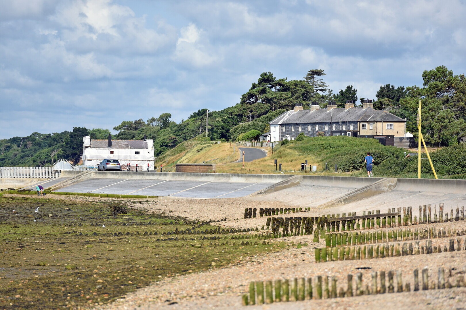 A coastal view with wooden groynes and a white cottage.