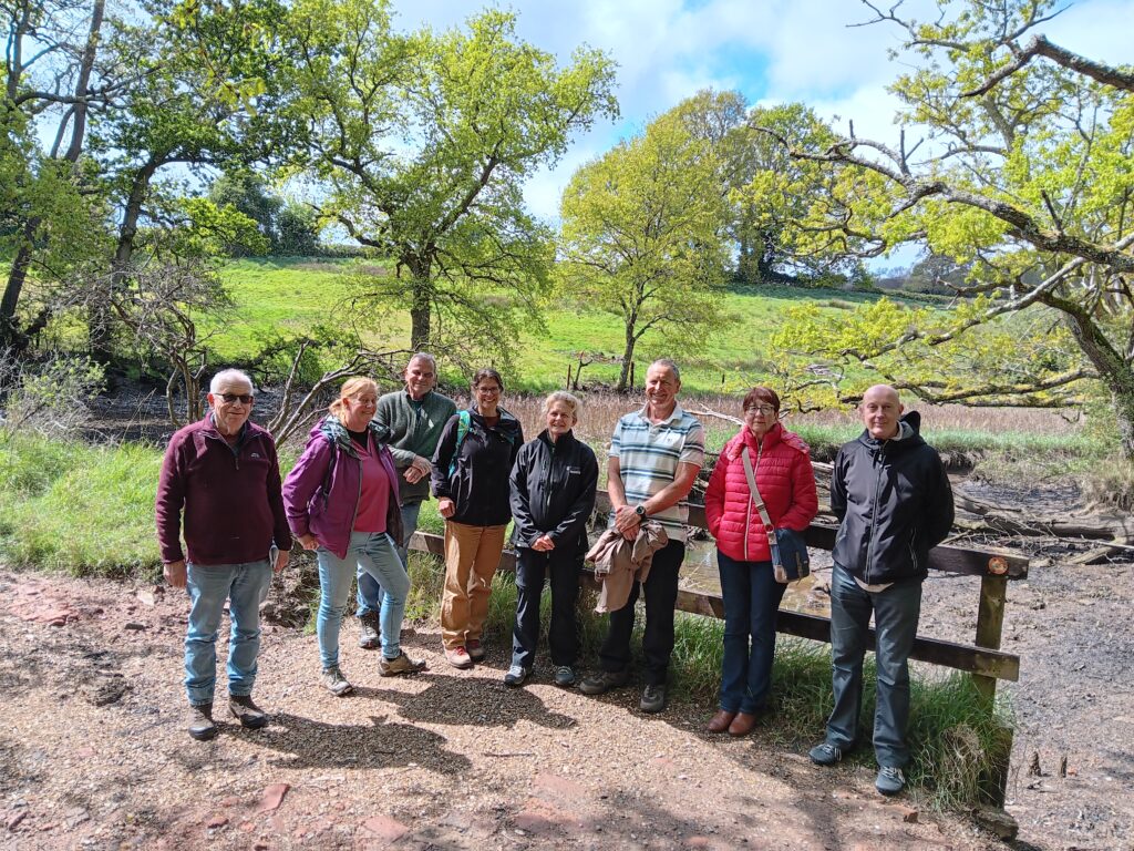 A group of eight people stand in a forest clearing in front of a wooden hand railing.