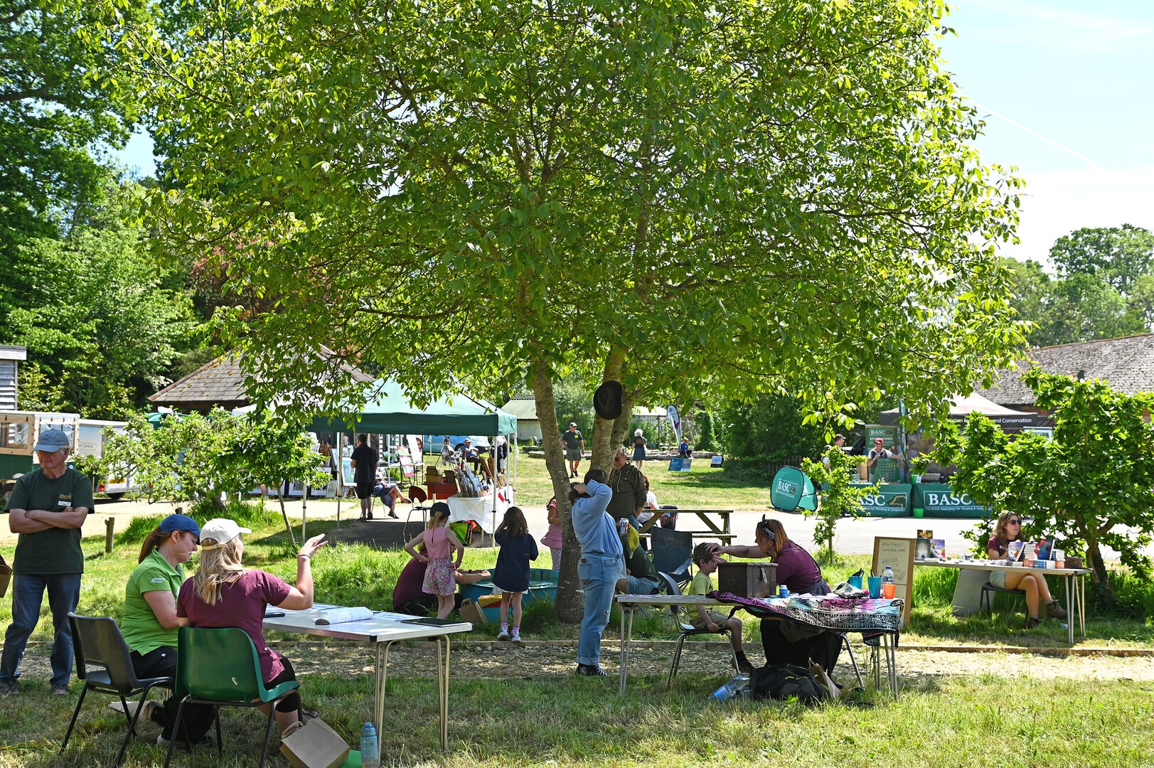 Conservation Awareness Day community event at the Countryside Education Trust. People stand and sit in a sunny area surrounded by trees.